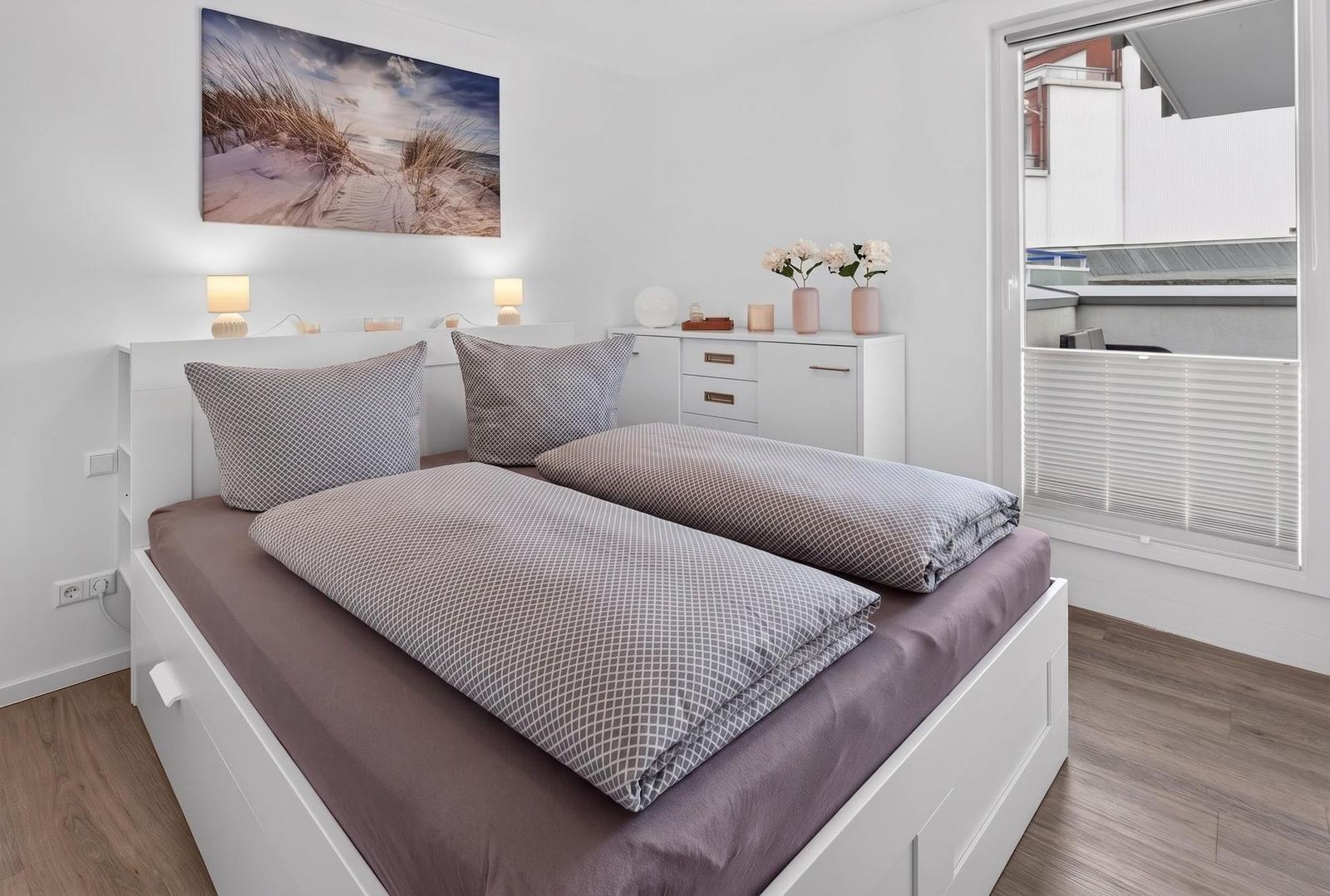 Schlafzimmer mit Doppelbett, weißen Möbeln und Blick auf Balkon.