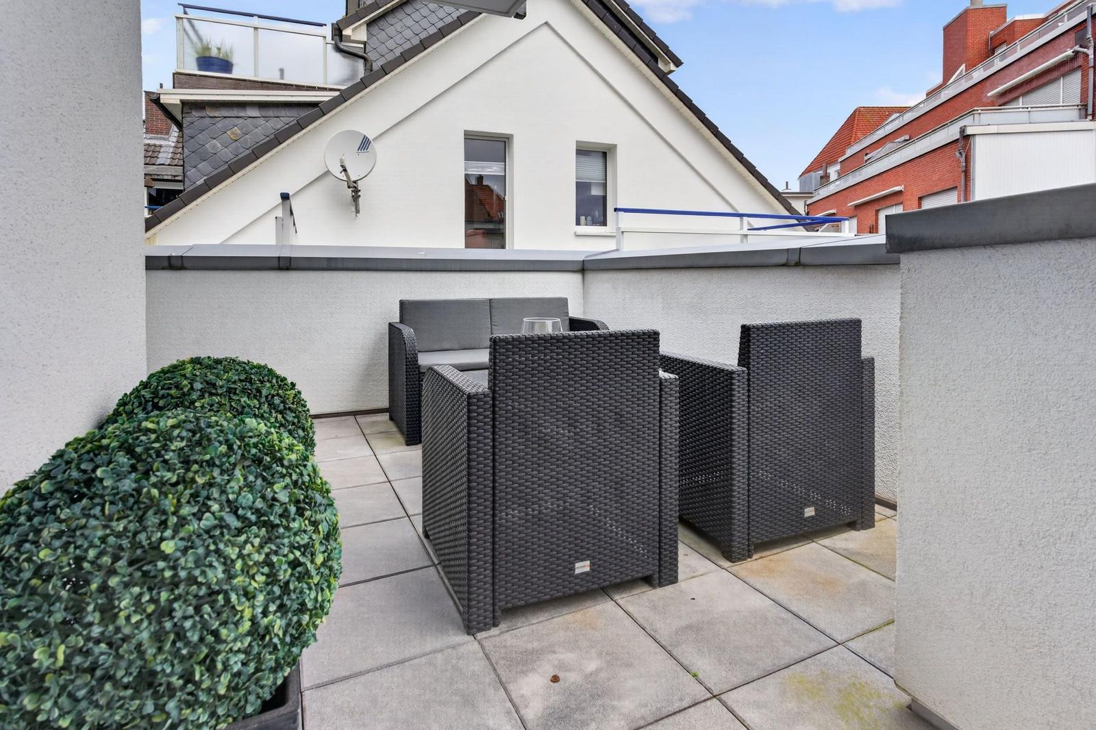 Terrasse mit Gartenmöbeln und Topfpflanze. Blick auf benachbarte Gebäude.