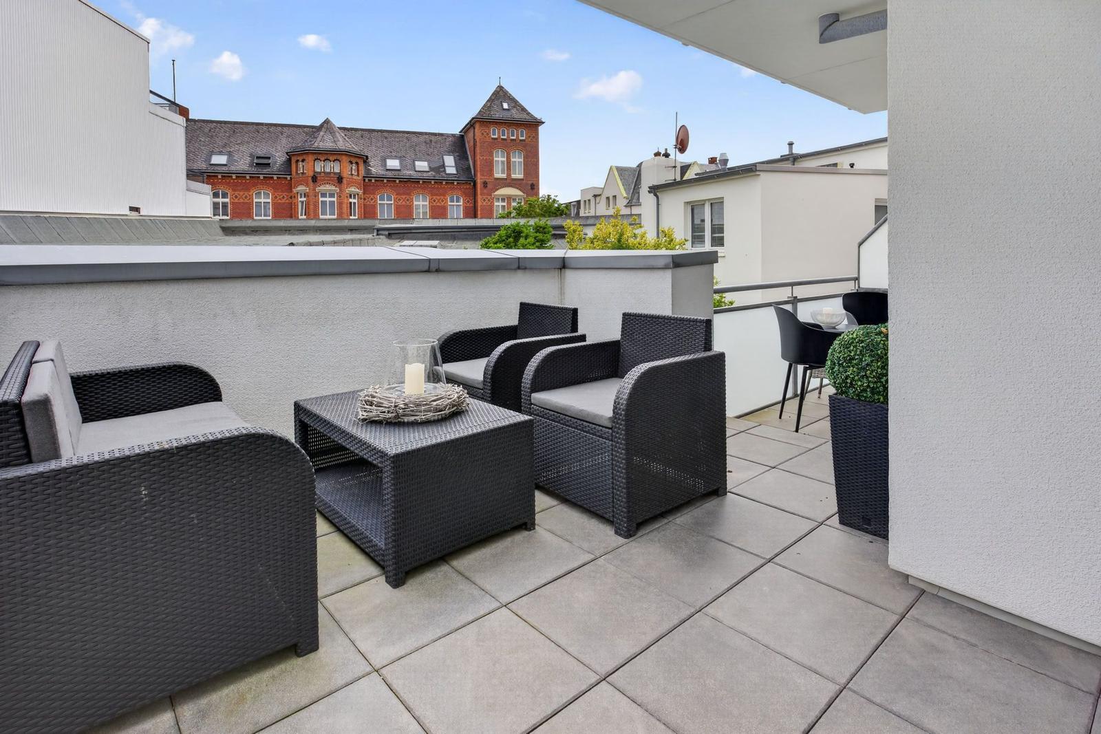 Terrasse mit Sitzgruppe und Blick auf ein rotes Gebäude.