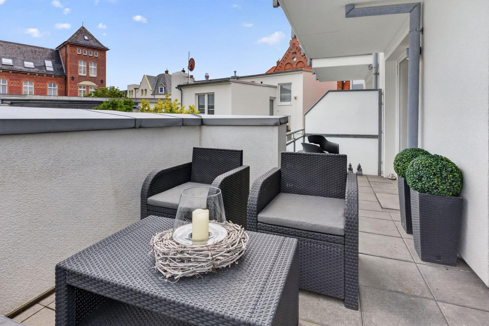 Terrasse mit zwei Sesseln, Tisch und Pflanzen. Blick auf umliegende Gebäude.