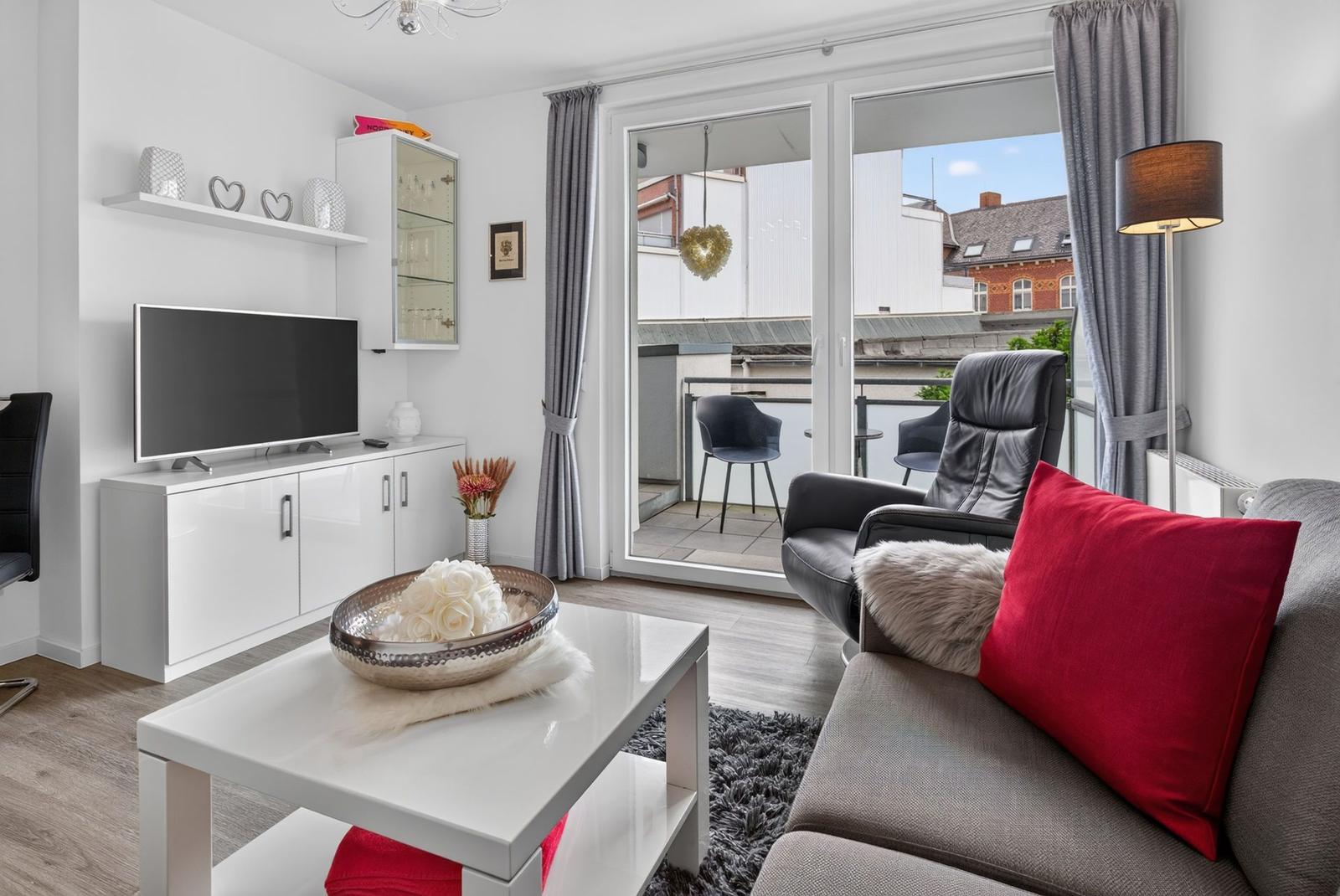 Wohnzimmer mit Sofa, Couchtisch und Balkon. Fernseher und Schrank sind vorhanden.