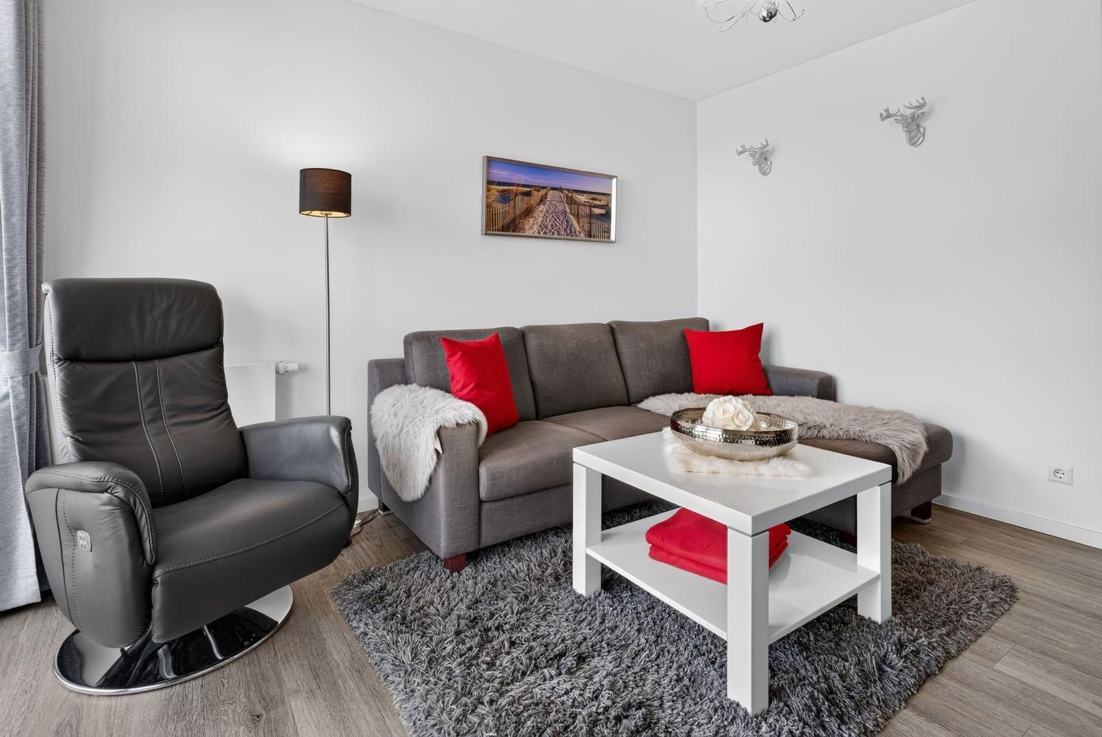 Wohnzimmer mit grauem Sofa, roten Kissen und schwarzer Relax-Sofa