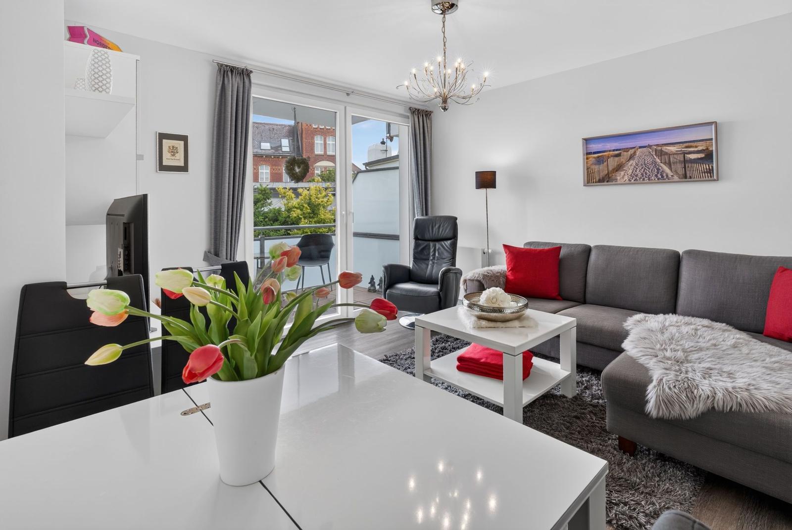 Wohnzimmer mit grauem Sofa, roten Kissen und Blick auf Balkon.