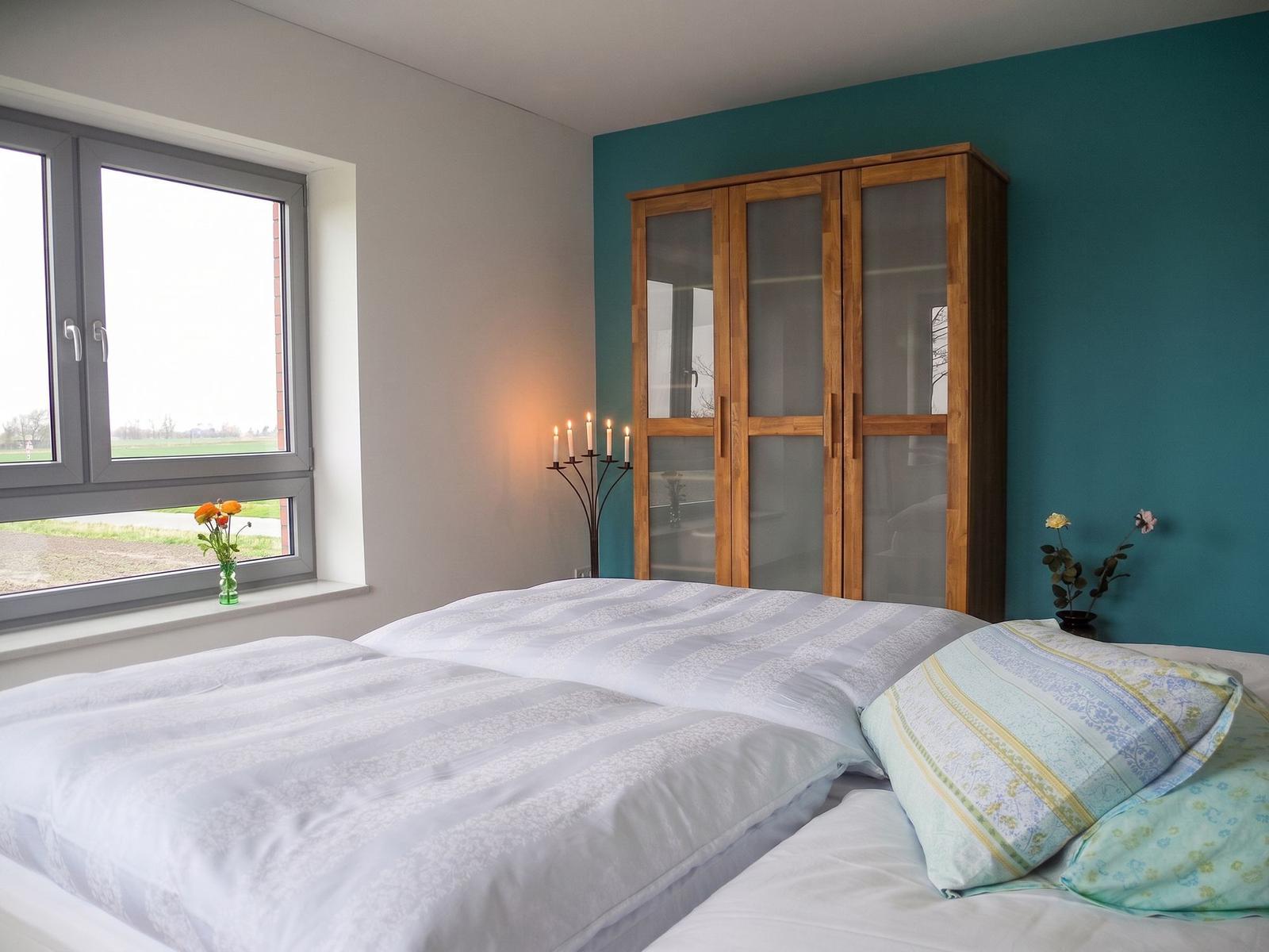 Schlafzimmer mit Bett, Kleiderschrank und Sofa. Fenster mit Blick auf Feld.
