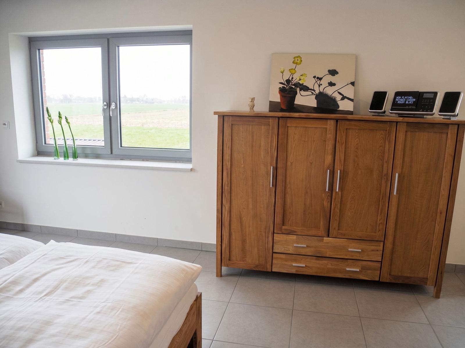 Zimmer mit Bett, Tisch, Stuhl und Bücherregal. Fenster mit Blick auf Feld.
