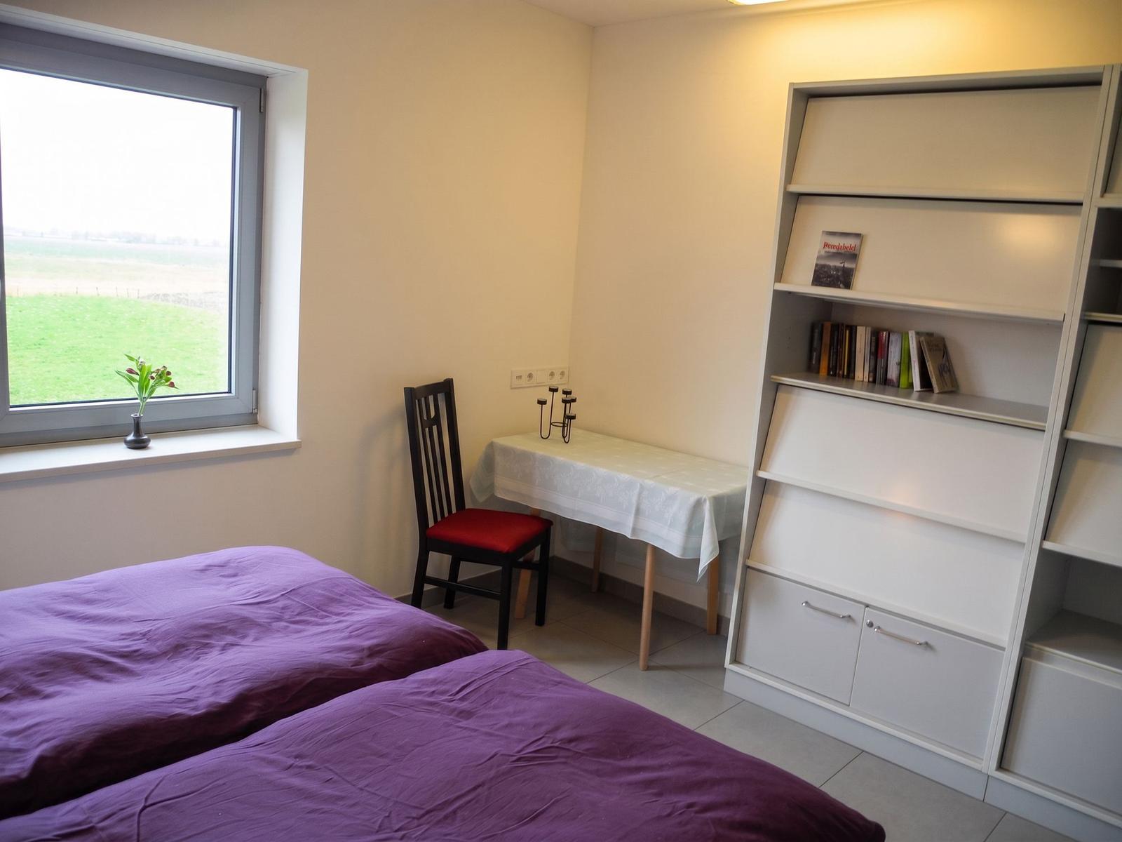Schlafzimmer mit Bett, Nachttisch und Fenster. Blick auf Felder.