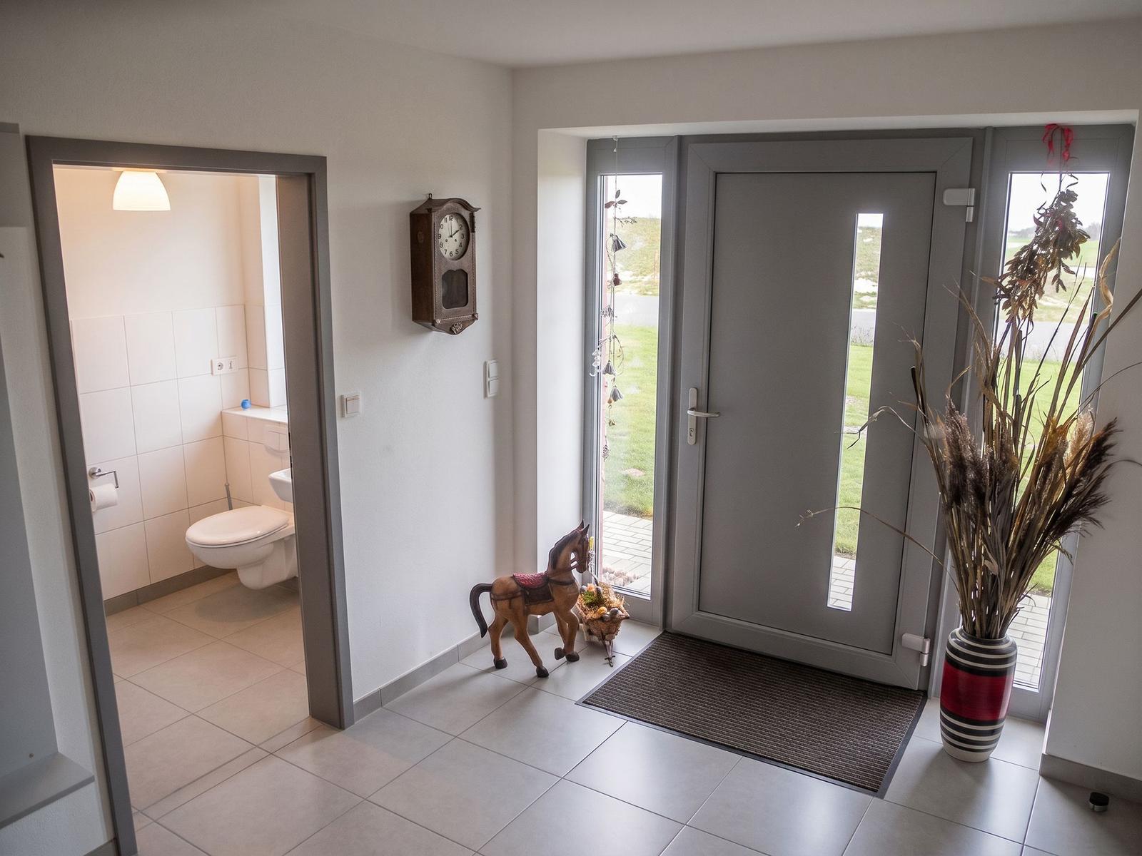 Eingangsbereich mit Garderobe, Uhr und Blick in einen Raum mit blauem Schrank.