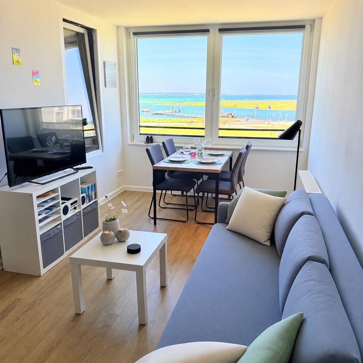 Wohnzimmer mit Sofa, Esstisch und TV. Blick auf Hafen und Meer.