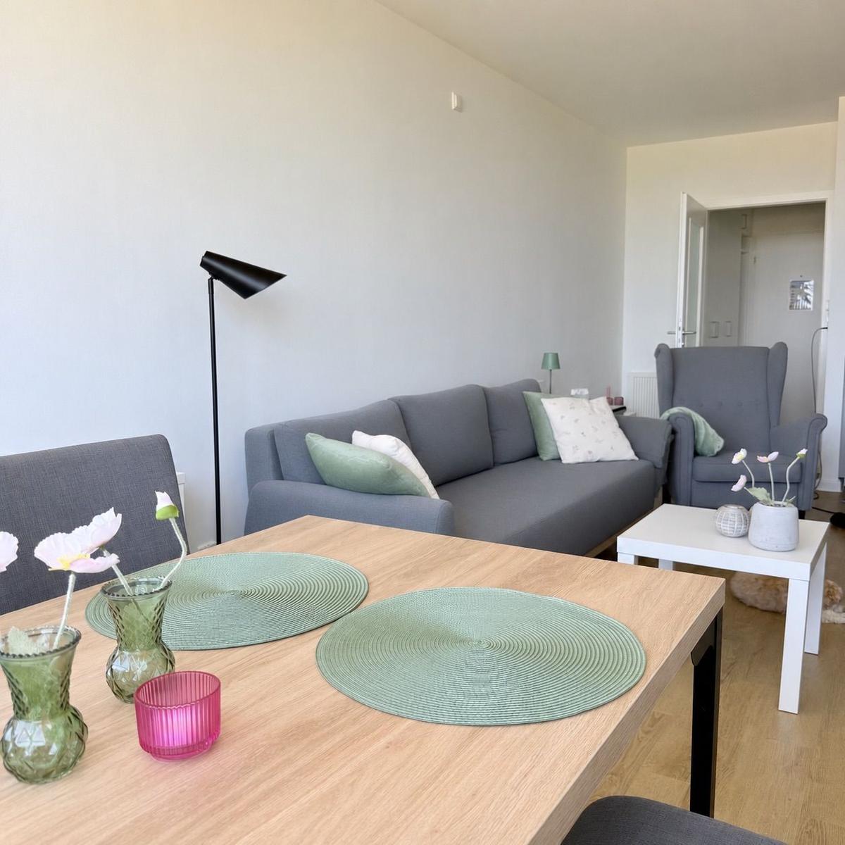 Ein Essbereich mit Holztisch und grauen Stühlen. Hinter dem Tisch ein grauer Sofa mit Kissen.