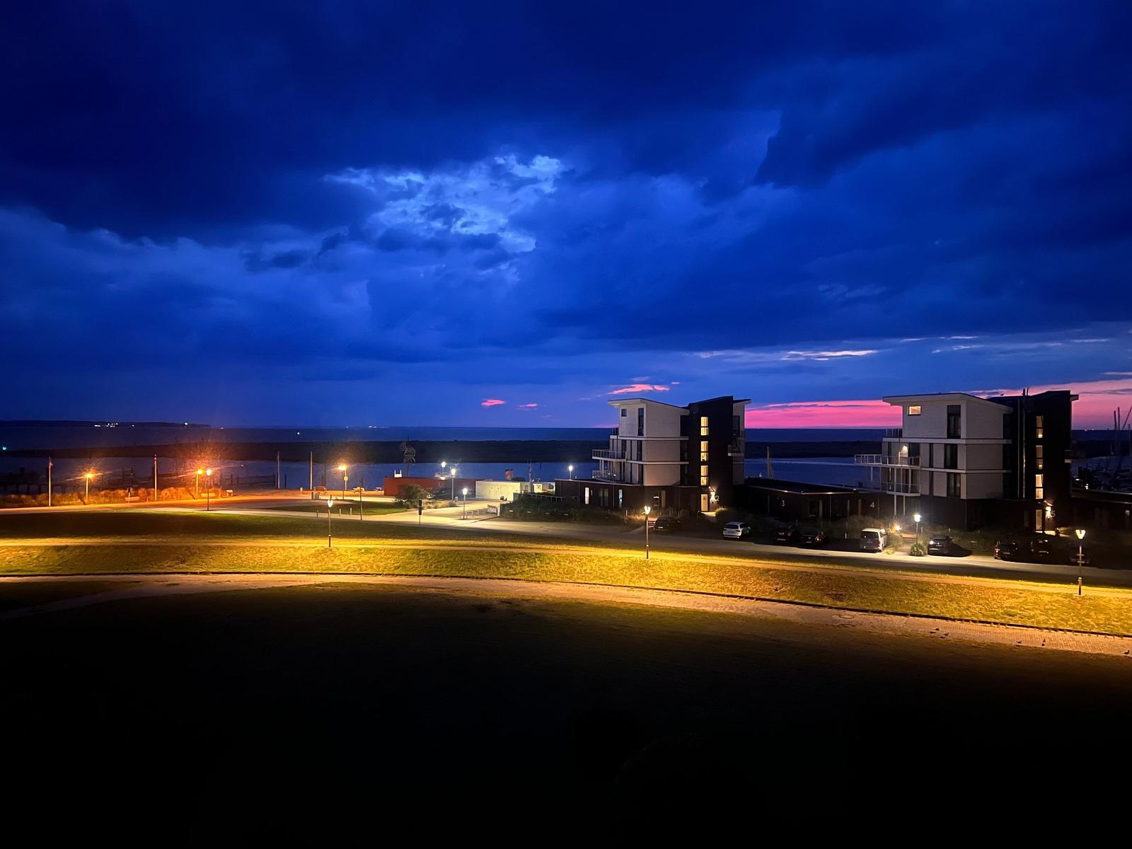 Modernes Gebäude bei Nacht mit Blick auf das Wasser und dramatischem Himmel.