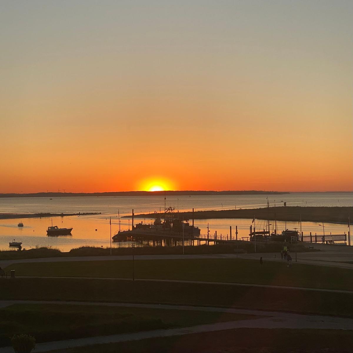 Sonnenuntergang über dem Hafen mit Booten und Steg im Vordergrund.