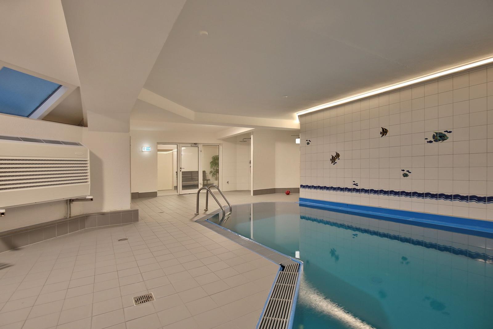 Innere Schwimmhalle mit blauem Wasser und dekorierten Wänden.