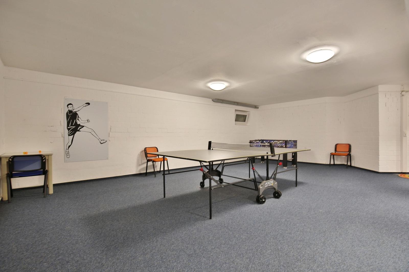 Raum mit Tischtennisplatte, Stühlen und Wandbild.
