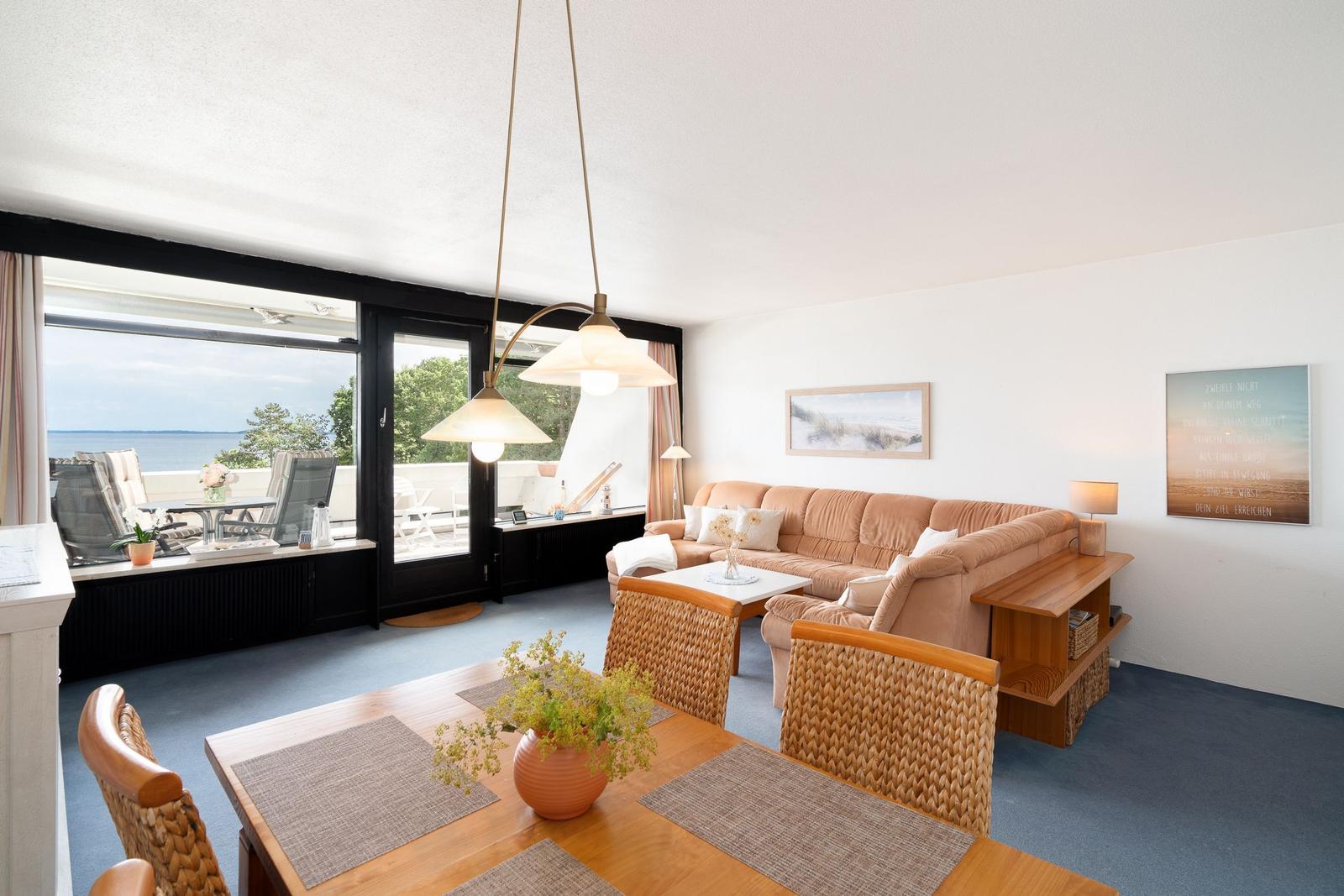 Wohn- und Essbereich mit Blick aufs Meer und Terrasse. Holztisch, Sofa und Wandbilder.