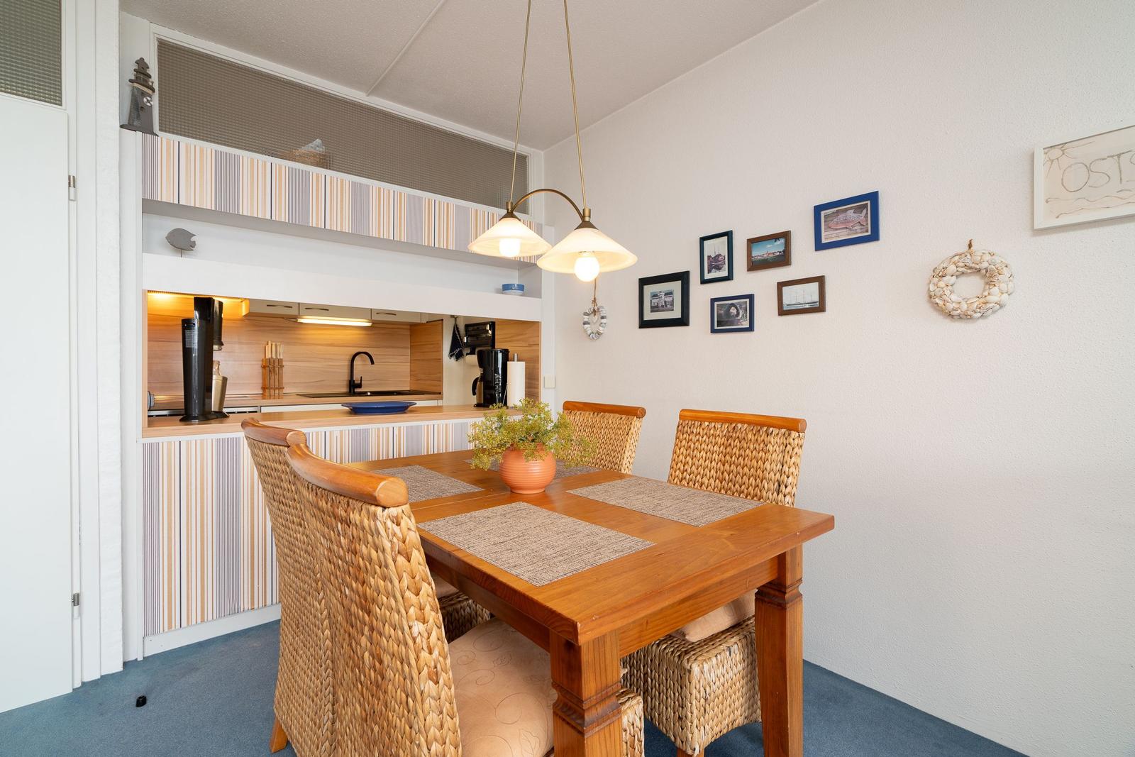 Essbereich mit Holztisch, Stühlen und Küchenbereich im Hintergrund.