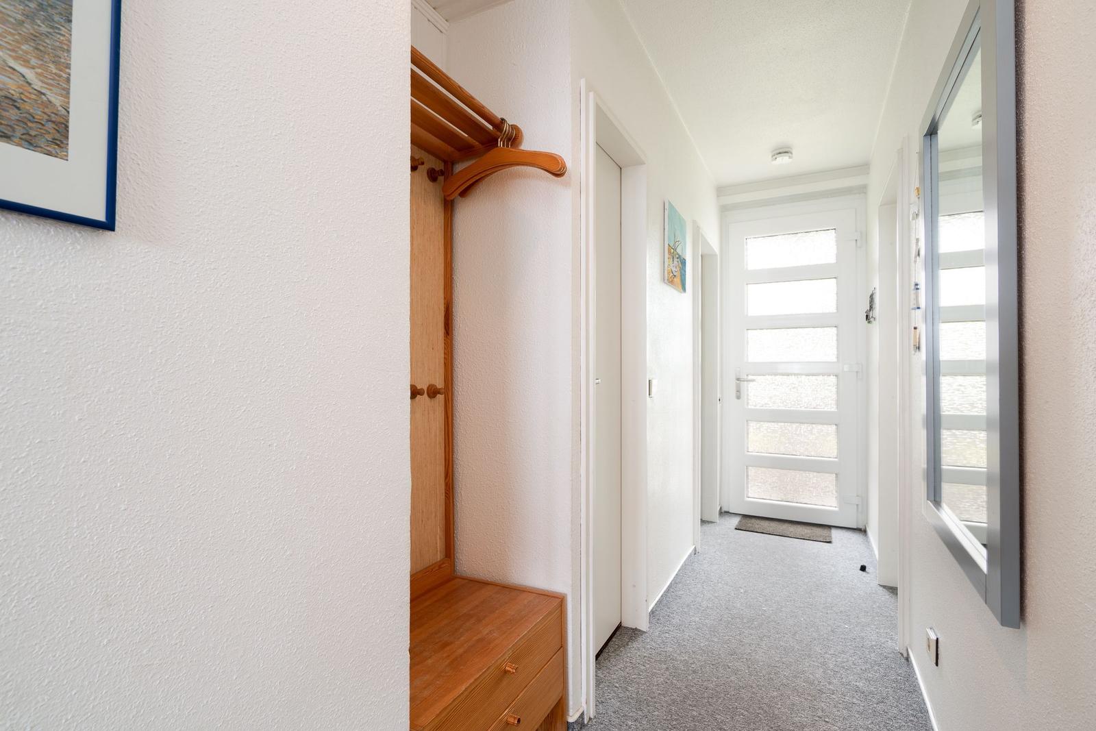 Flur mit Holzgarderobe, Tür und Fenster. Teppichboden und weiße Wände.
