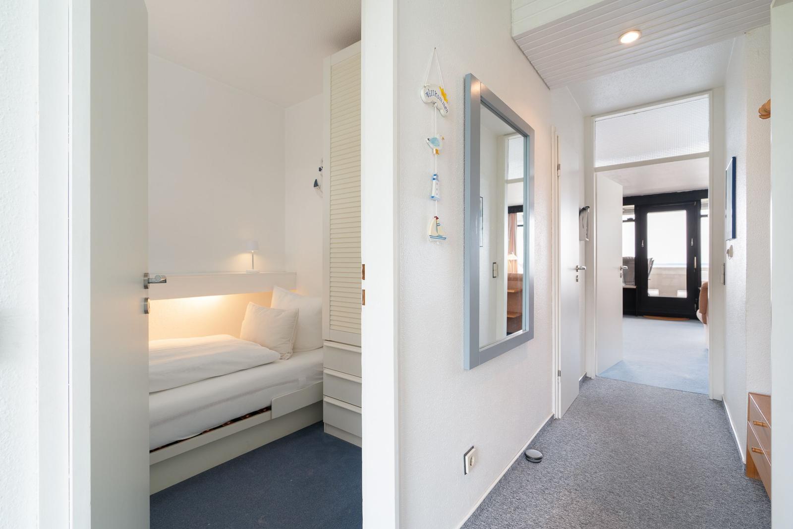 Schlafzimmer mit Bett und Kleiderschrank. Flur mit Spiegel und Tür zum Wohnbereich.