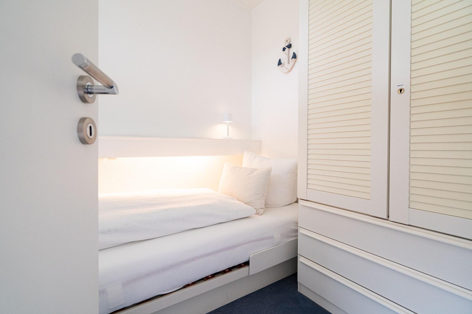 Schlafzimmer mit weißem Bett, Kleiderschrank und Ankerdekoration an der Wand.