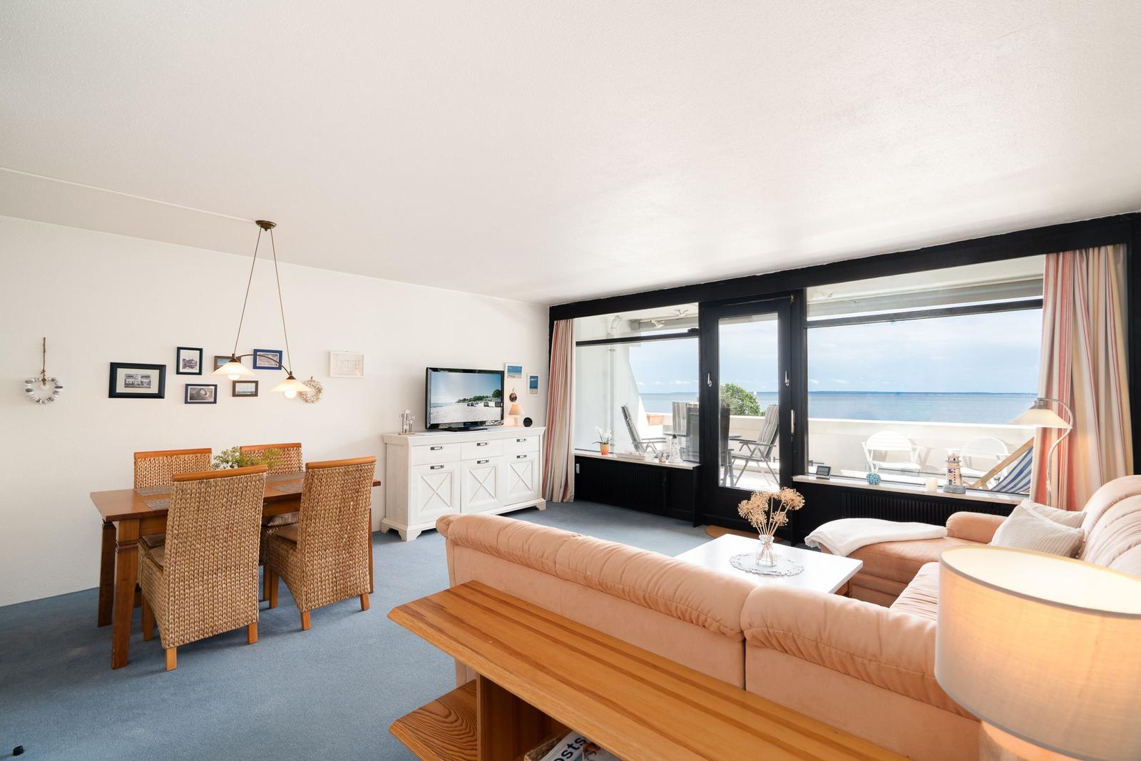 Wohn- und Essbereich mit Meerblick und Balkon. Sofa, Esstisch und TV.