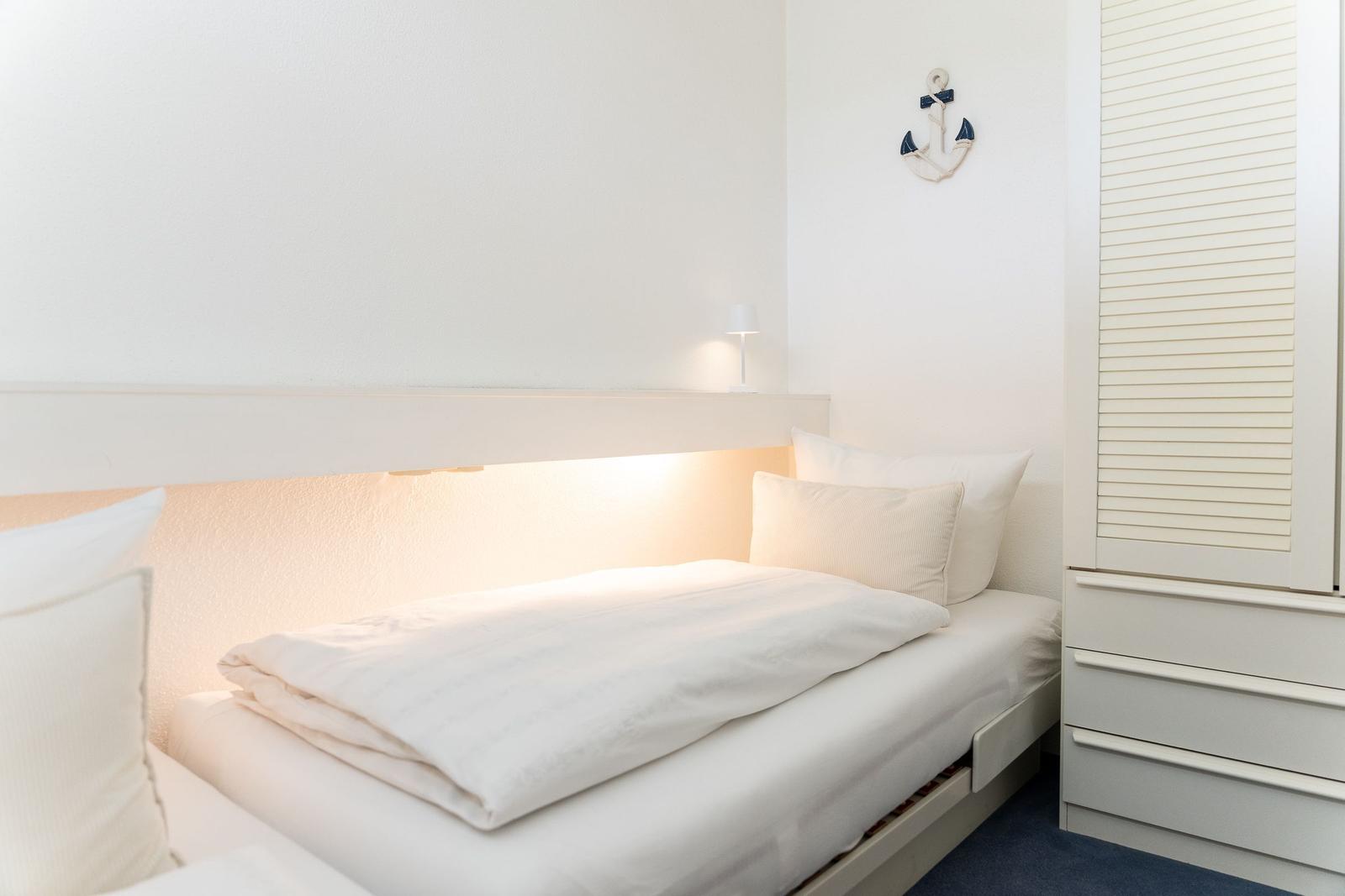 Schlafzimmer mit Bett, Nachttisch und Garderobe. An der Wand hängt ein Anker.