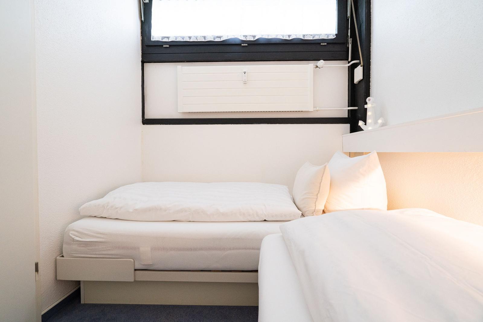 Schlafzimmer mit weißem Bett und Fenster mit Jalousie.
