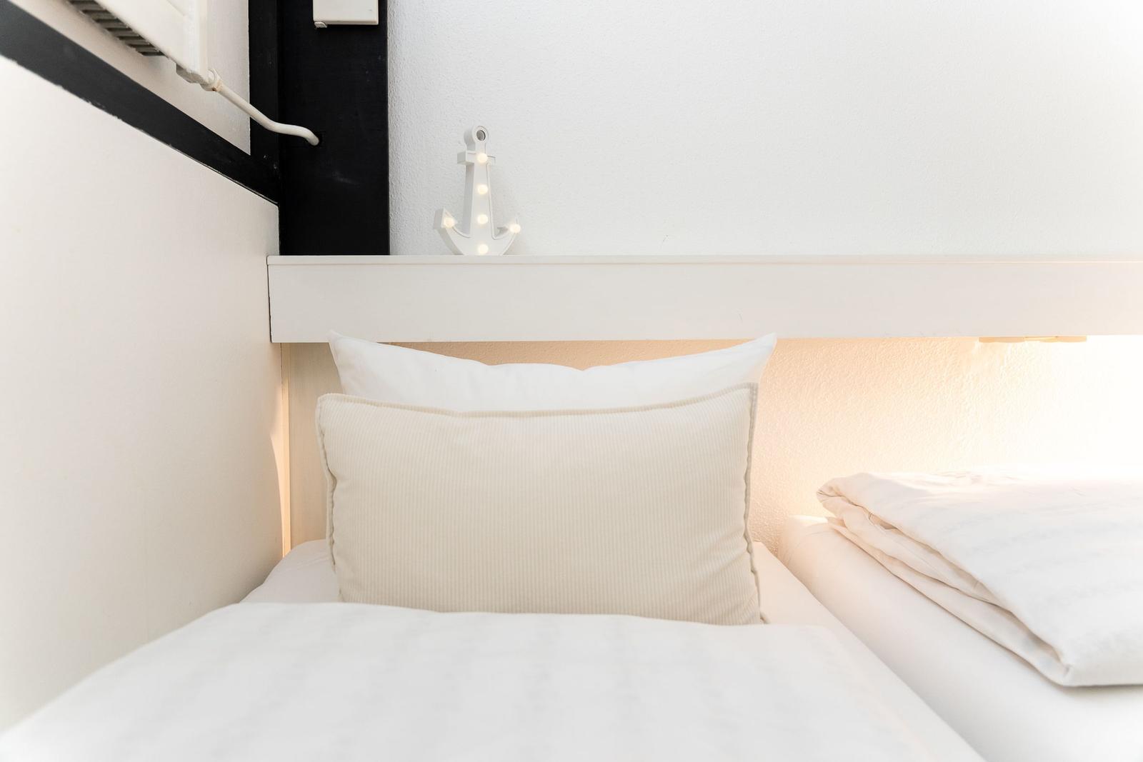Schlafzimmer mit weißem Bett, Kissen und Anker-Dekoration an der Wand.