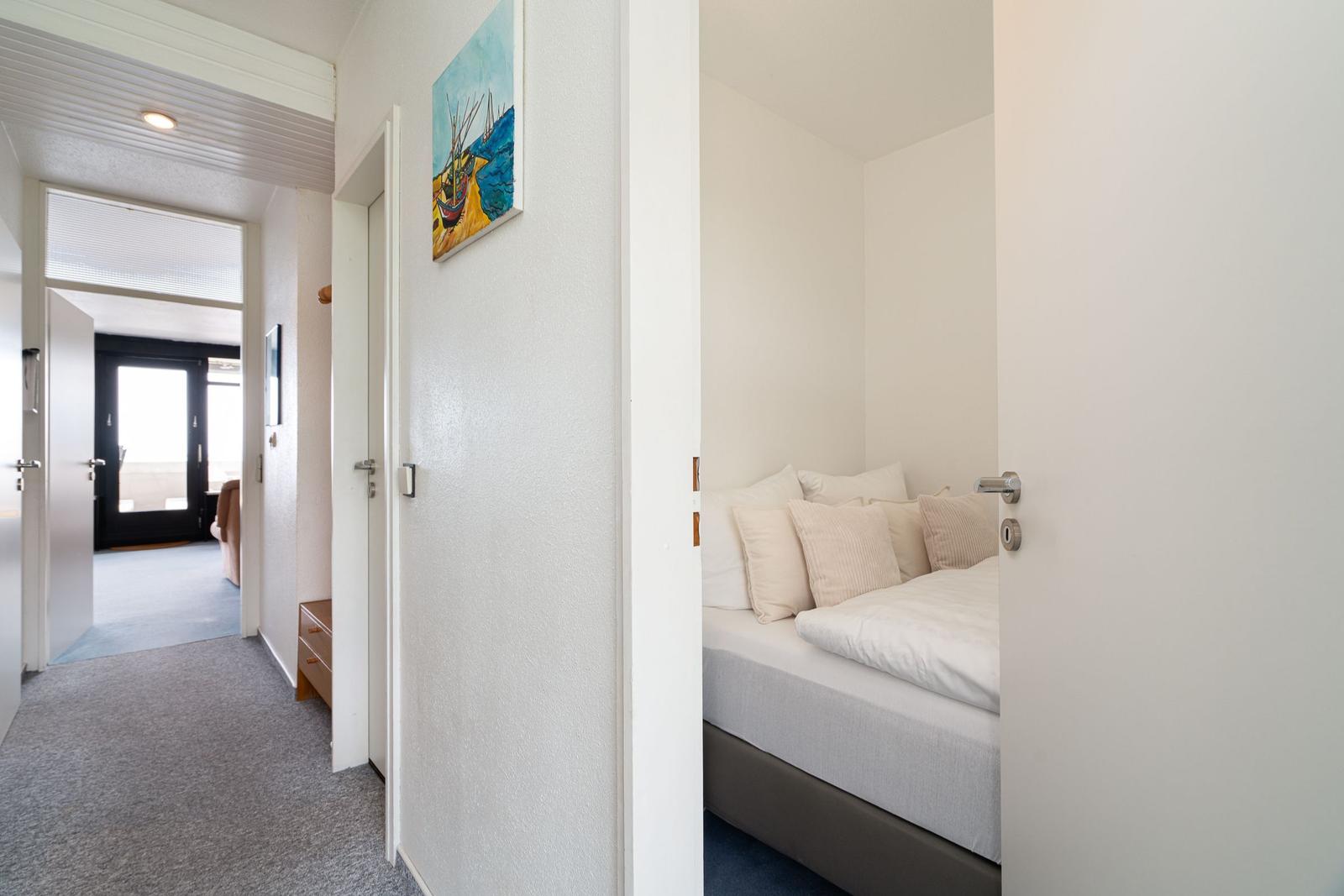 Schlafzimmer mit Bett und Kissen. Flur mit Bild an der Wand und Türöffnung.
