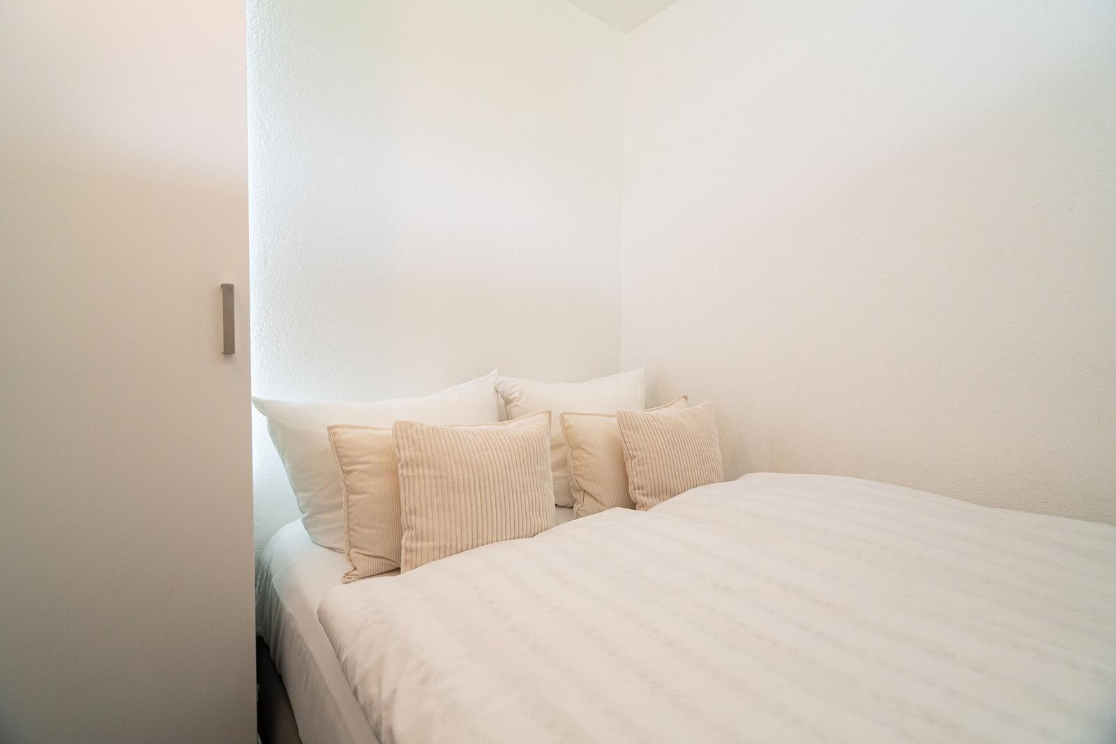 Schlafzimmer mit Bett, Kissen und weißen Wänden.
