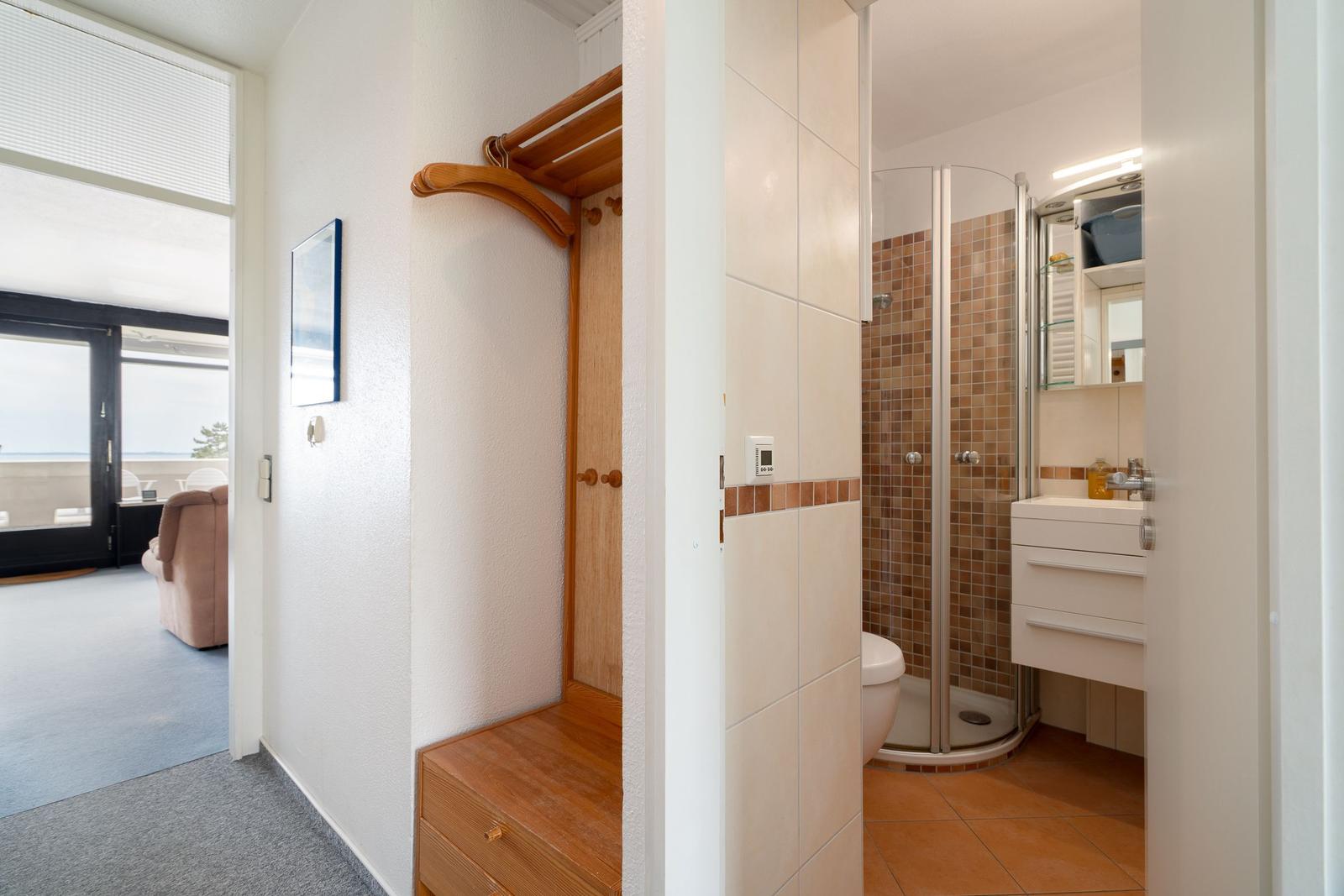 Badezimmer mit Dusche und Waschbecken. Blick in Wohnbereich mit Balkon.