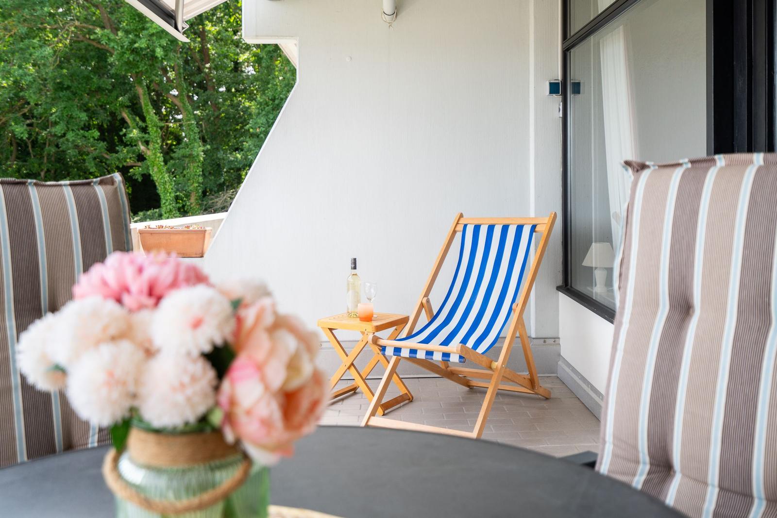 Terrasse mit Liegestuhl, Tisch und Blumen im Vordergrund.