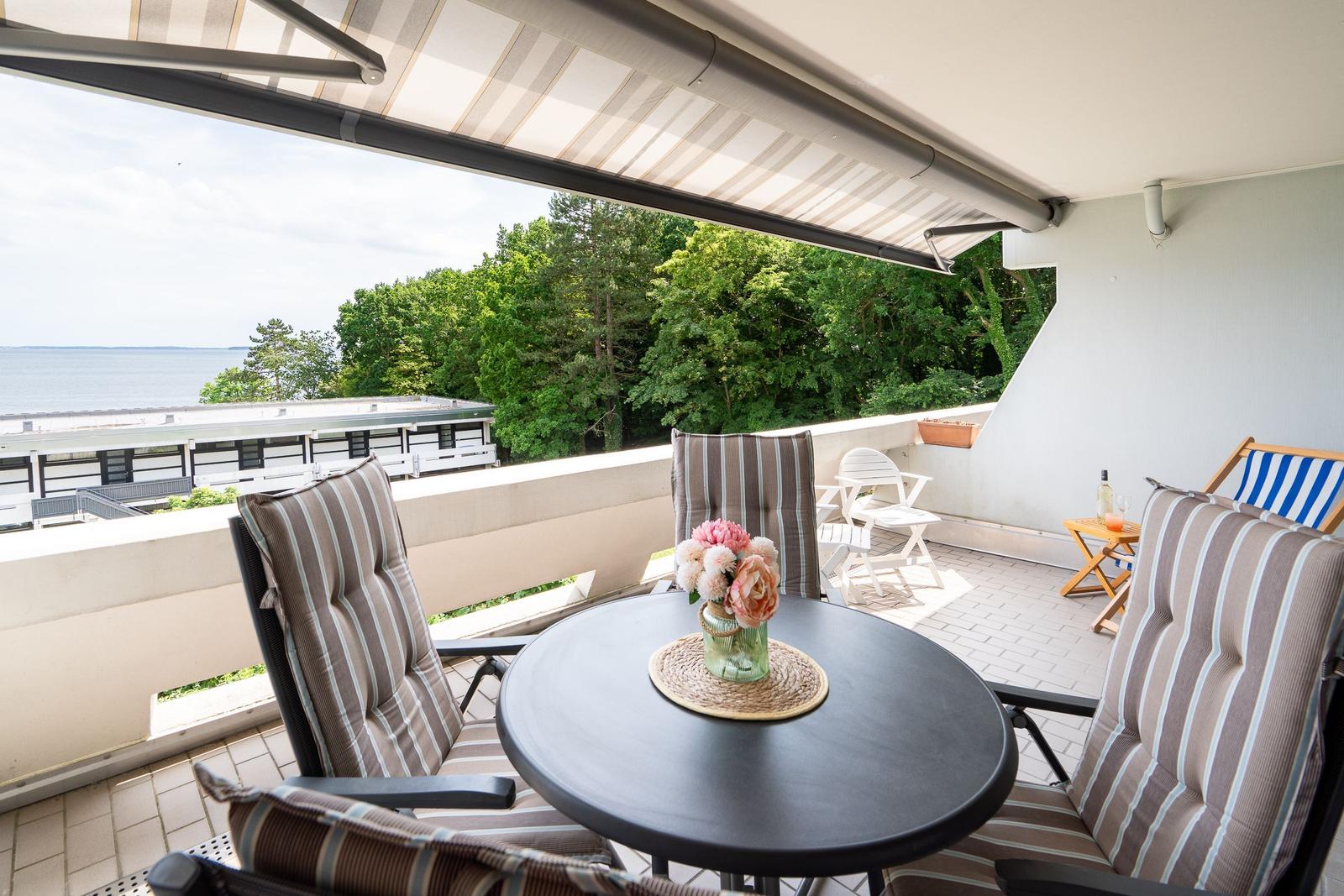 Terrasse mit Tisch, Stühlen und Blick auf Wasser und Bäume.