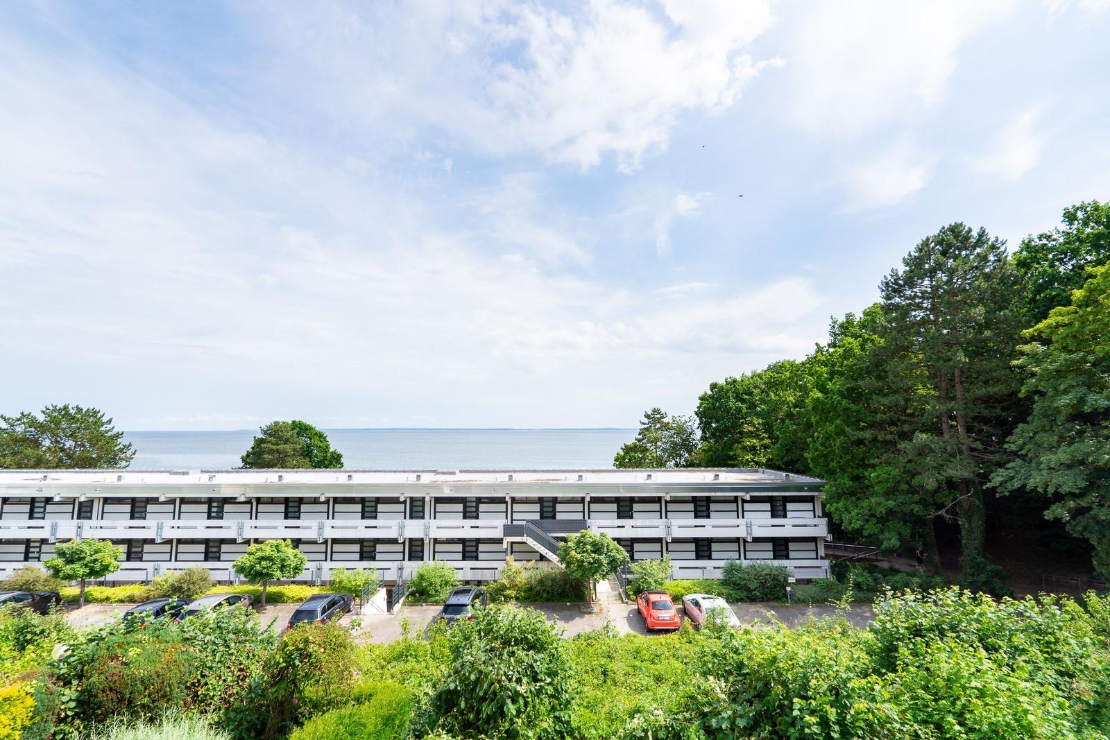Ferienhaus mit Blick aufs Meer, umgeben von Grün und Parkplätzen.