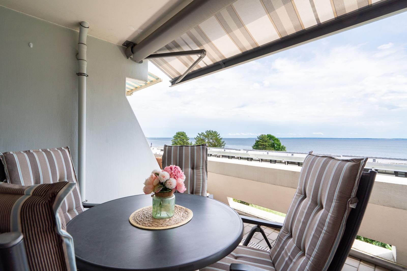 Balkon mit Tisch, Stühlen und Meerblick unter Markise.