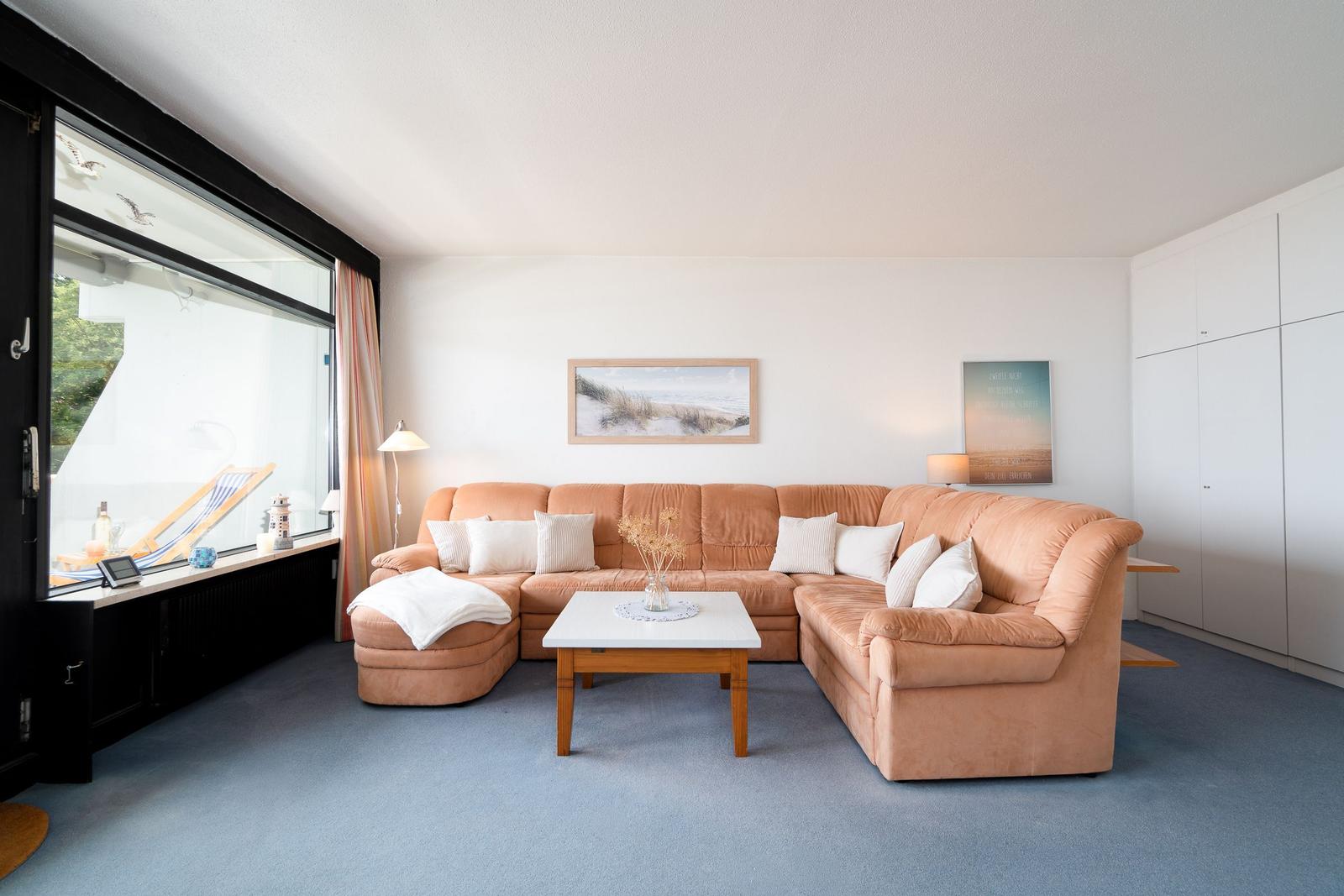 Ein Wohnzimmer mit orangefarbenem Sofa, Tisch und Fensterblick.