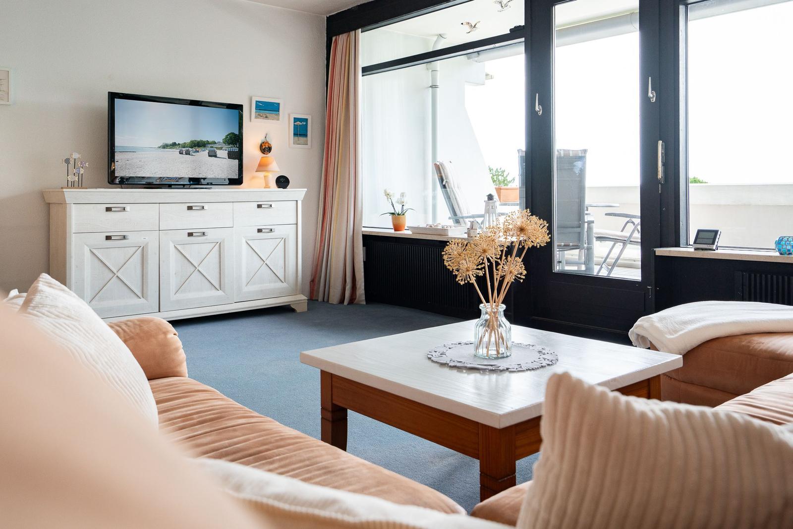Wohnzimmer mit Sofa, Couchtisch und TV. Durchgang zur Terrasse mit Sitzgelegenheiten.