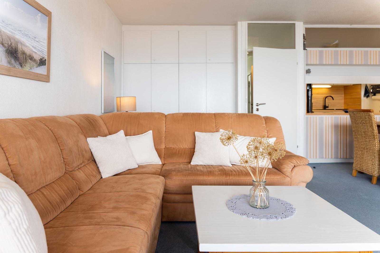 Wohnzimmer mit braunem Sofa, weißem Tisch und Küchenbereich im Hintergrund.