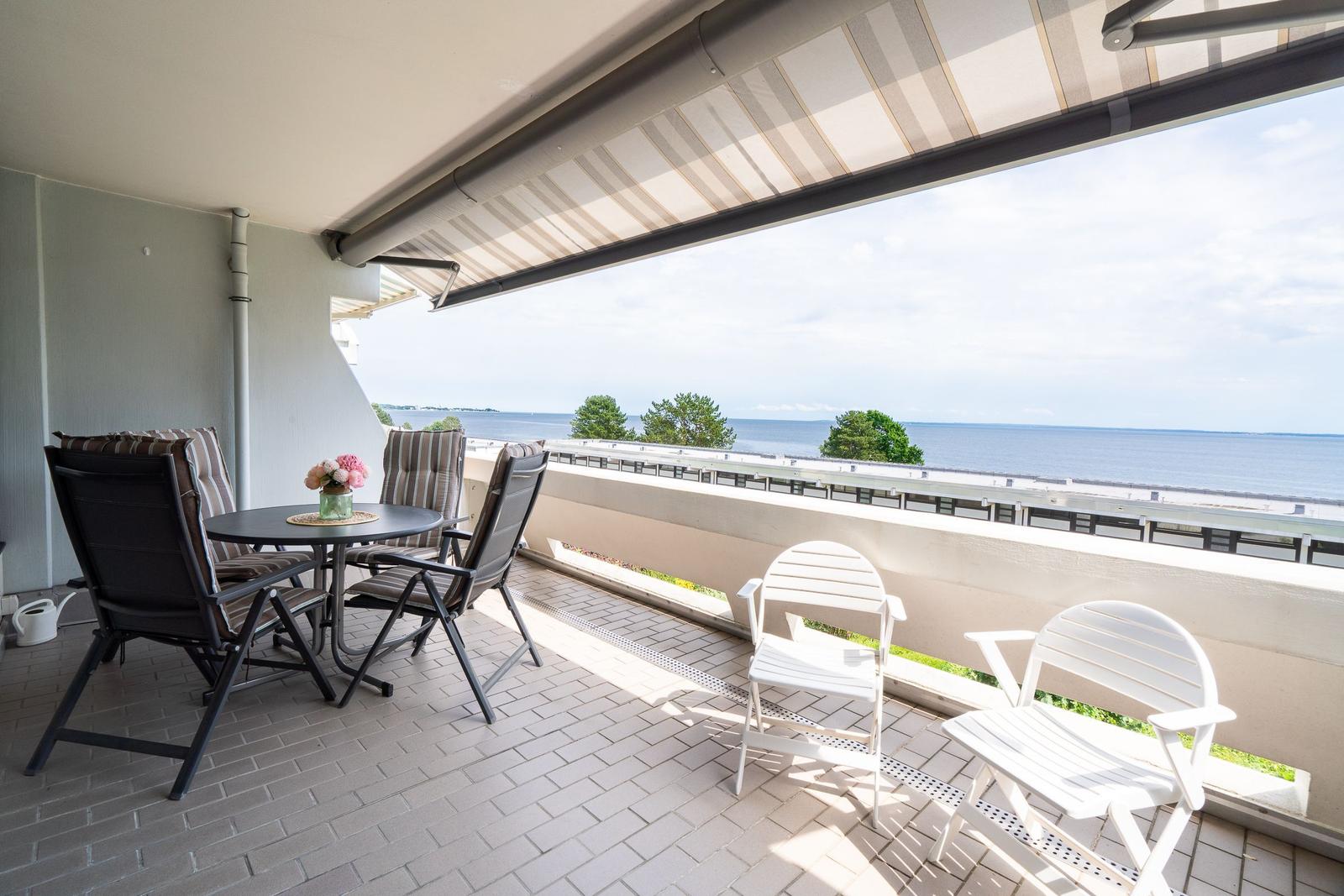 Terrasse mit Sitzgruppe und Meerblick. Sonnenschutz und weiße Stühle.