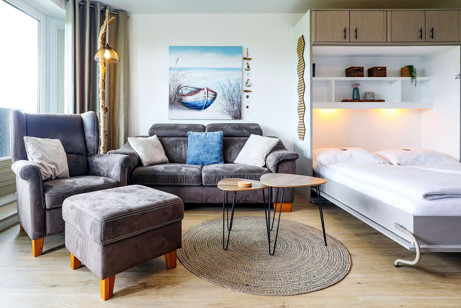 Wohnbereich mit Sofa, Sessel und Bett. Wandbild und Holzmöbel.