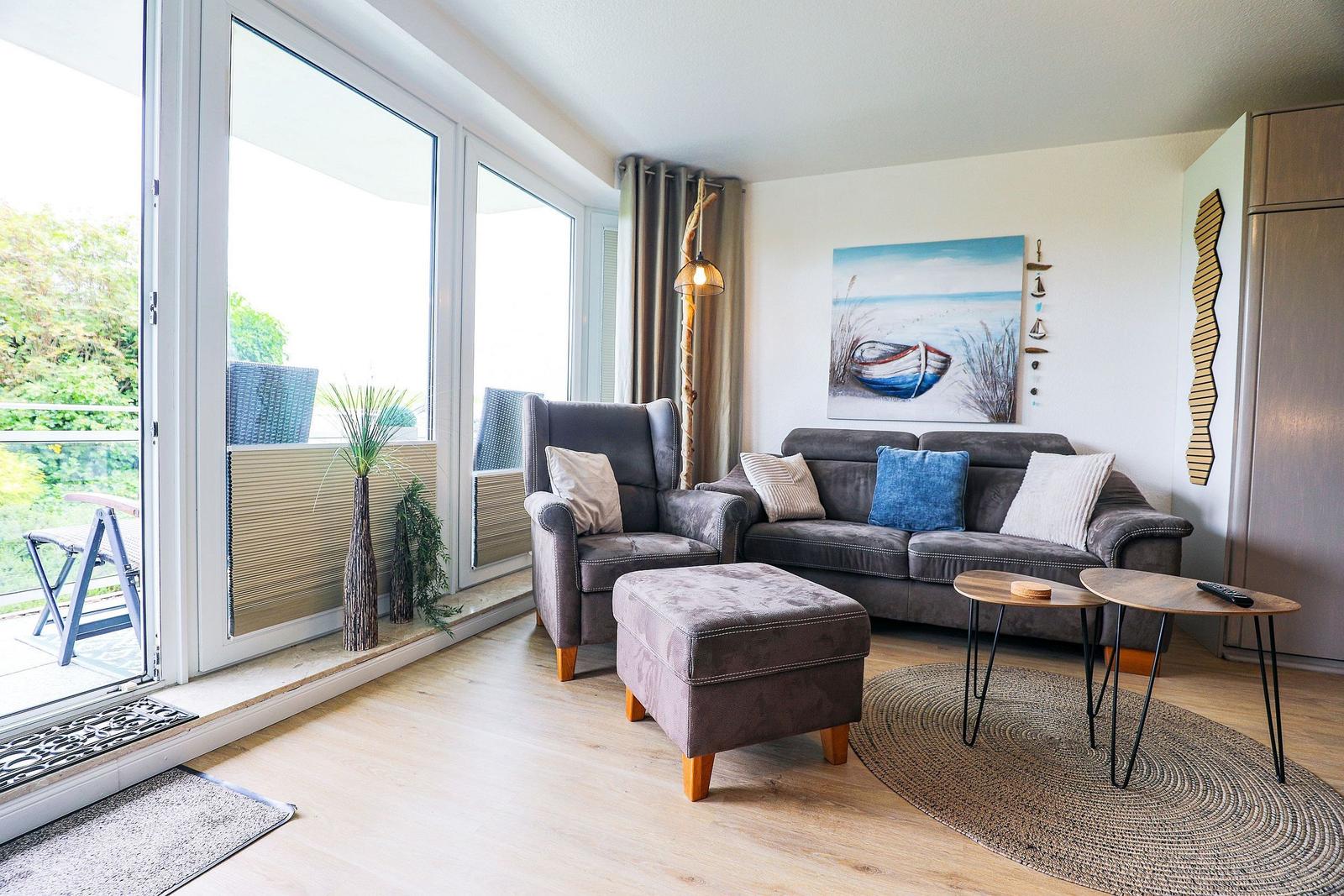 Wohnzimmer mit Sofa, Sessel und Blick auf Balkon