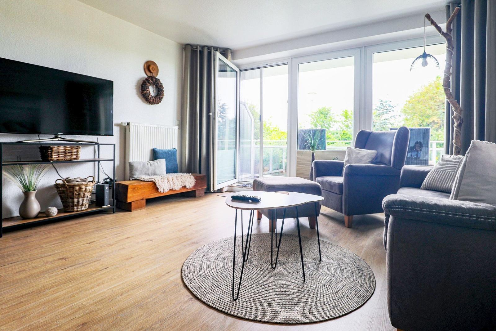 Wohnzimmer mit TV, Sitzgelegenheiten und Blick auf Balkon.
