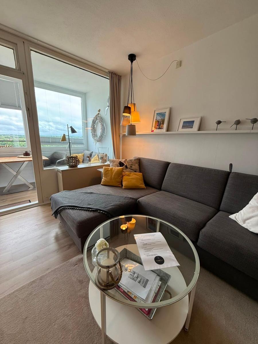 Ein Wohnzimmer mit grauem Sofa, Glas-Tisch und Blick auf Balkon.