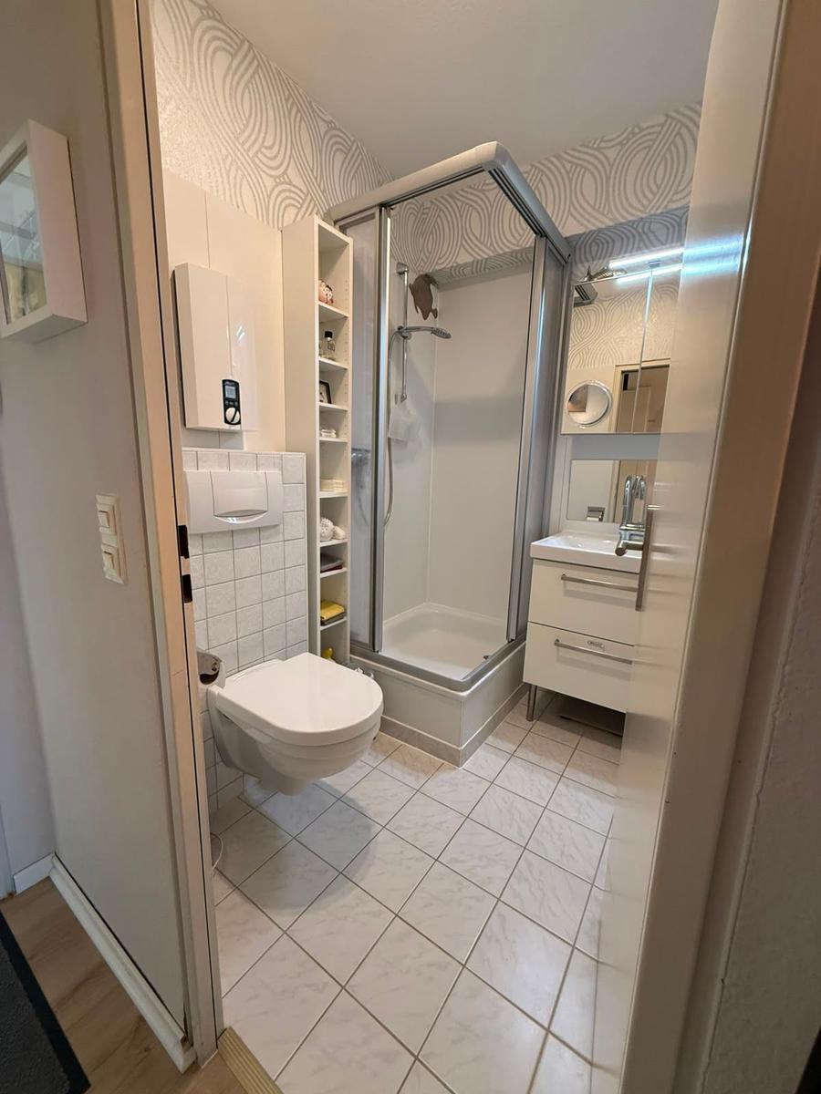 Badezimmer mit Dusche, Waschbecken und Toilette. Fliesenboden und Wandverkleidung.