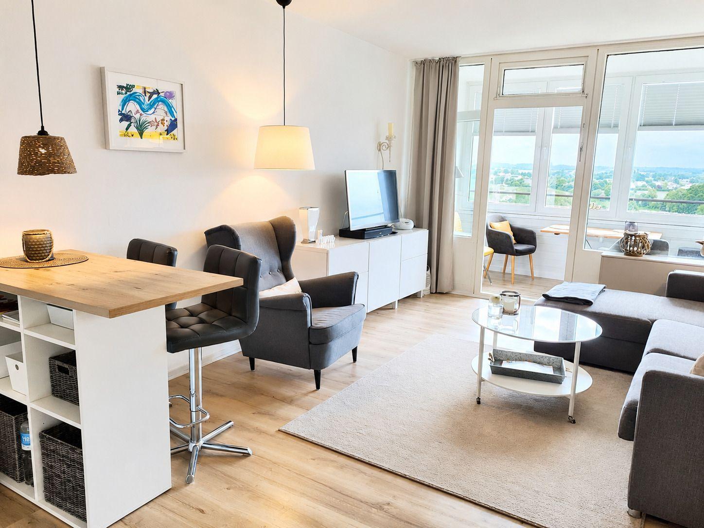 Wohnzimmer mit Essbereich, Sofa, TV und Balkon mit Blick.