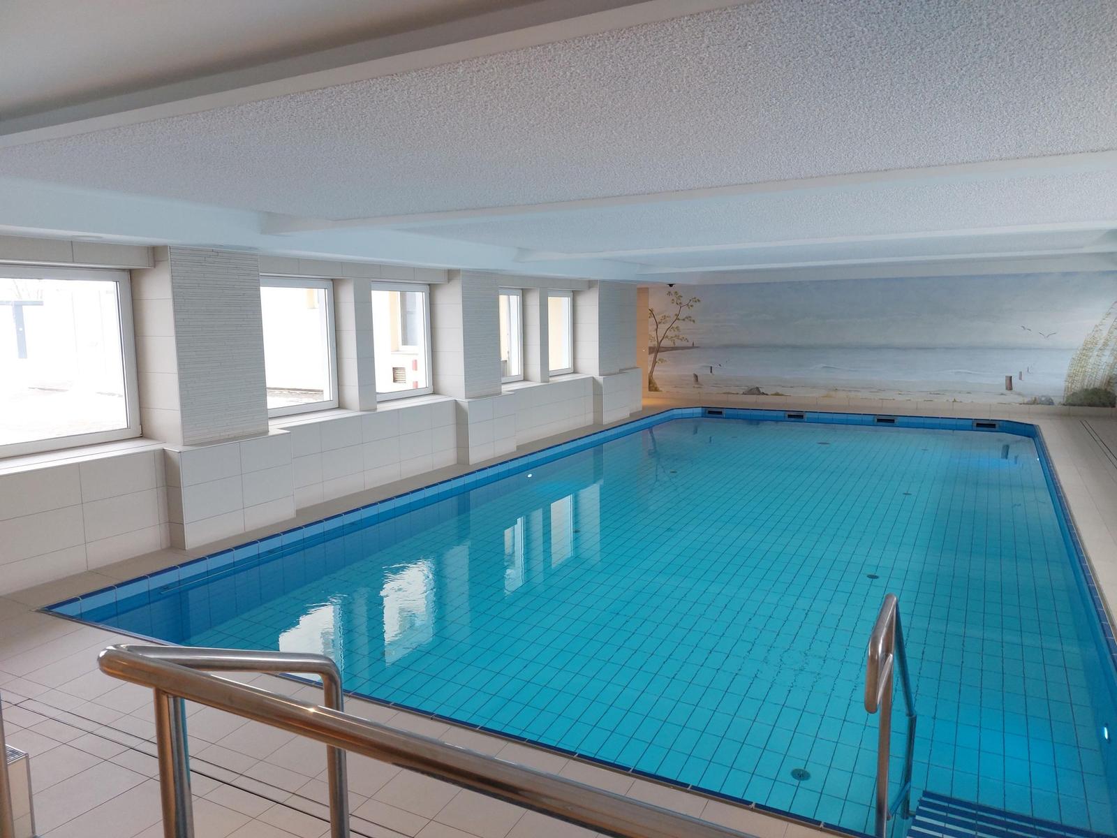 Indirektes Licht beleuchtet den Innenpool mit blauen Fliesen und Metallgeländern.