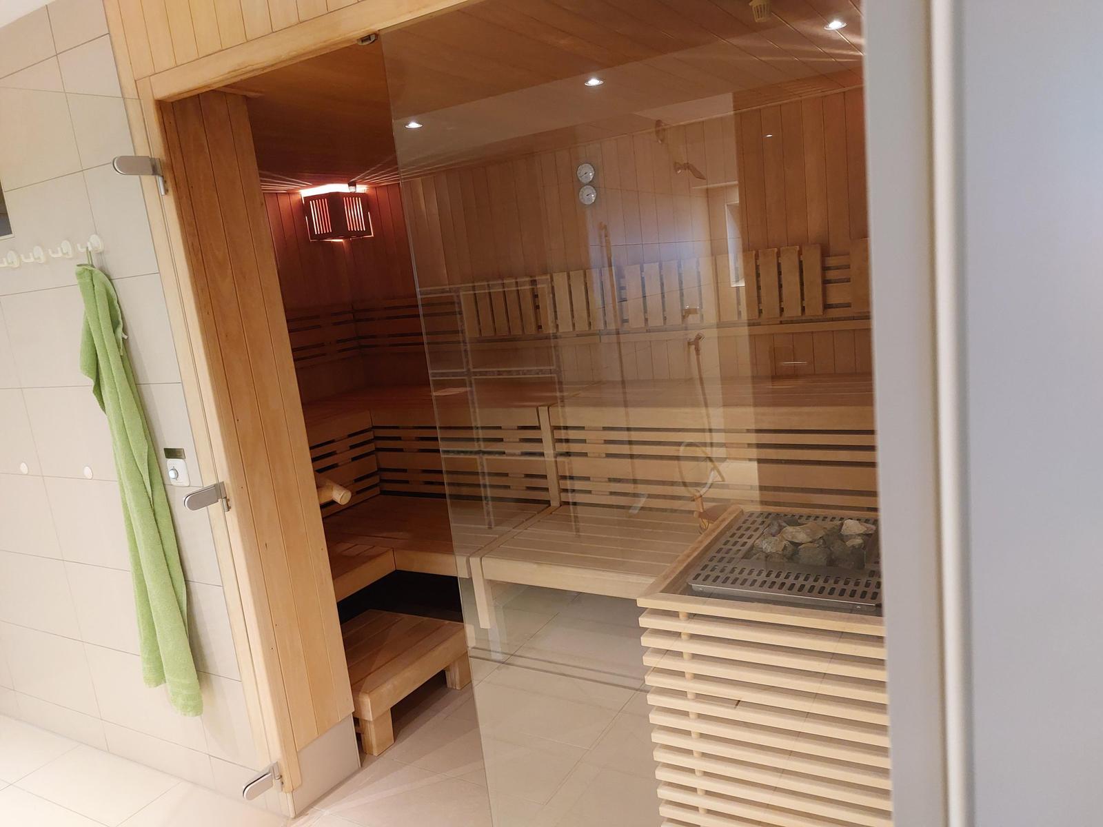 Sauna mit Holzbanken und Glaswand. Grüner Handtuch hängt an Wand.