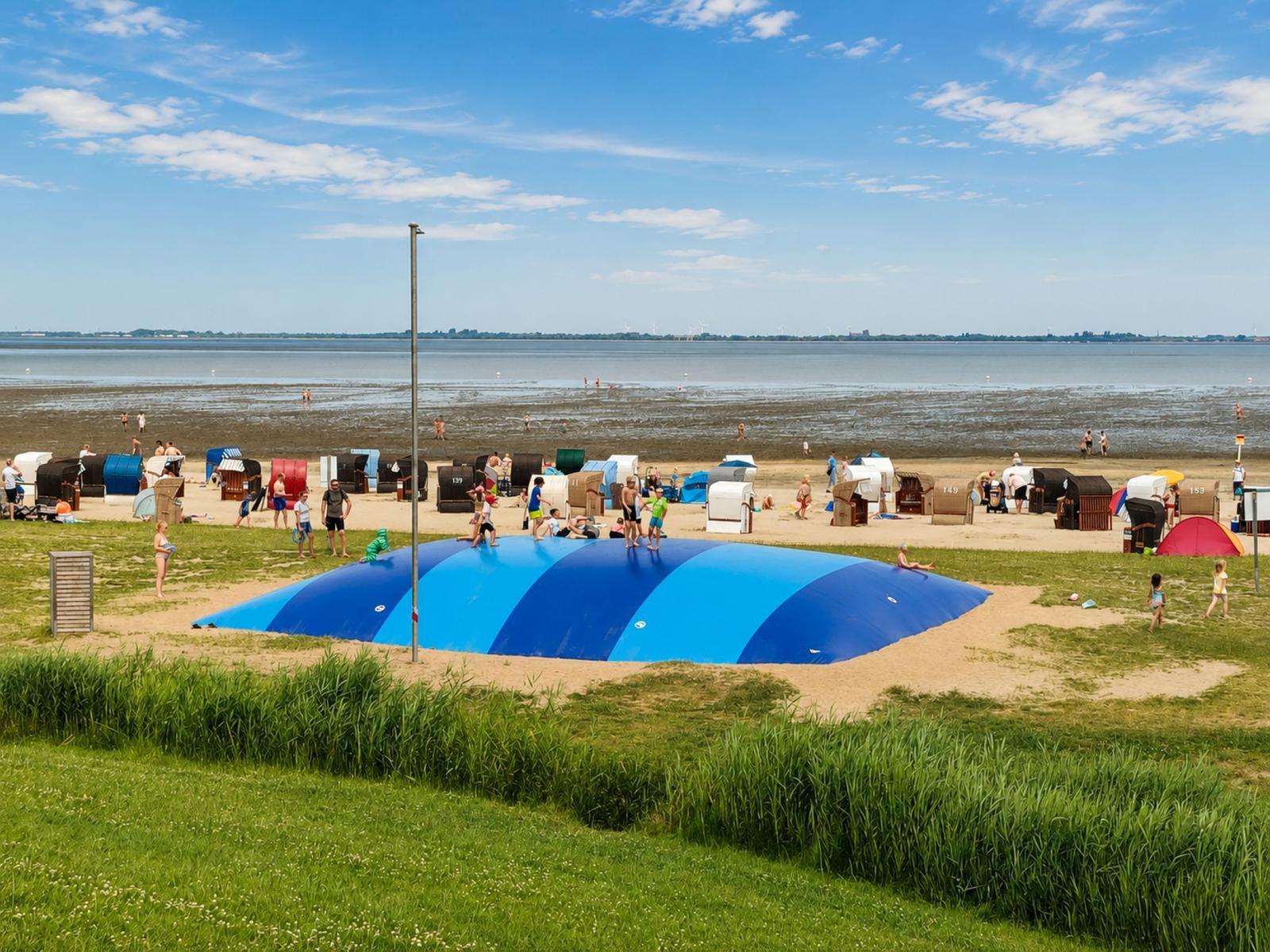 Strand mit bunten Strandkörben und blauem Springbecken. Menschen spielen und entspannen.