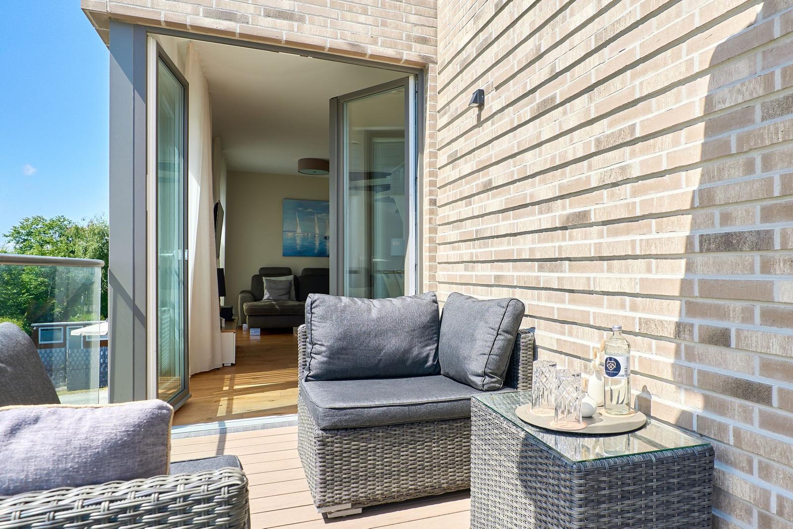 Terrasse mit Sitzgruppe und Tisch. Durchgehende Glastüren führen ins Wohnzimmer.