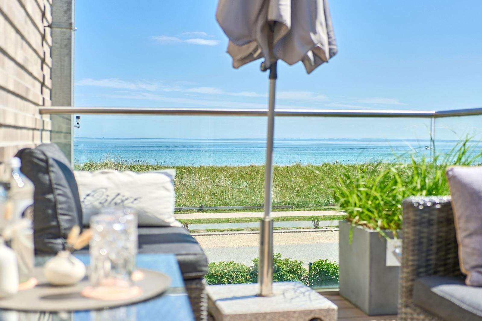 Terrasse mit Blick auf das Meer und Grasland. Sitzmöbel, Sonnenschirm und Pflanzen.