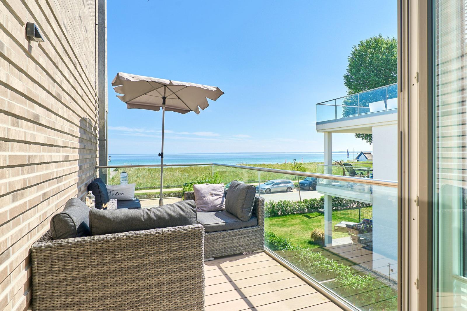 Terrasse mit Sitzgruppe und Sonnenschirm. Blick auf das Meer und grünen Garten.
