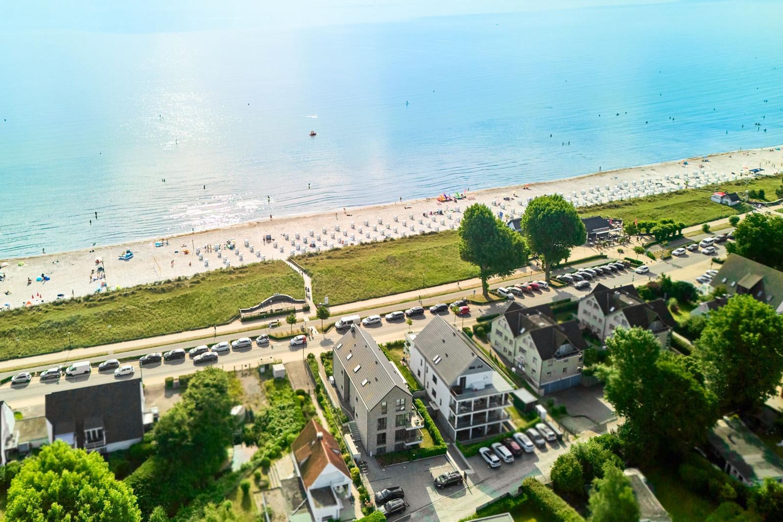 Aerial view of beach with rows of sun loungers, coastal road, and residential buildings.